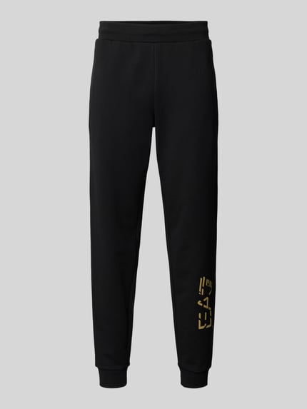Produktfoto, Sweatpants mit elastischem Bund und Label-Print von EA7 Emporio Armani in Schwarz, reine Baumwolle, Regular-Fit, glatte Textur, Label-Print in Gold, elastischer Bund, Innenbeinlänge 78 cm bei Größe M.