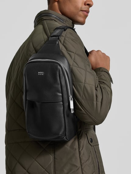 Männermodel trägt Umhängetasche in Leder-Optik Modell 'Ray EVO_Monostrap' von BOSS, schwarz, feine Struktur, Ganzkörperansicht von vorne, Herren Umhängetasche von BOSS