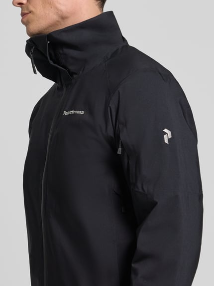 Männermodel trägt zwarte Heren jack met capuchon Model 'Maroon' van Peak Performance, regular fit, labelstitching, ritssluiting, ruglengte maat M 75 cm, schouderbreedte 47 cm, borstwijdte 57 cm, mouwlengte 69 cm, detailopname rechterbovenlichaam.