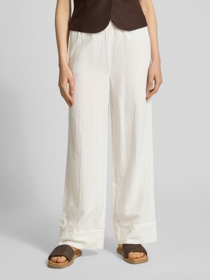 Frauenmodel trägt Relaxed Fit Weite Hose aus Baumwoll-Viskose-Mix von Tom Tailor Denim, Optik:Unifarben, Muster: Gestreift, Materialverarbeitung: Seersucker, seitliche Eingrifftaschen, Tunnelzug, Bundabschluss: Elastisch, Farbe: Weiß, Struktur: leicht gecrinkelt, Ganzkörperansicht von vorne.