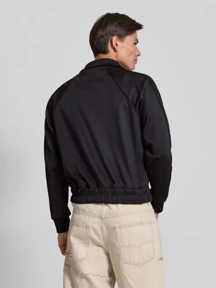 Männermodel trägt schwarze Sweatjacke mit Stretch-Anteil von RHUDE, elastischer Material-Mix, Raglanärmel, Boxy Fit, Ganzkörperansicht Rückansicht.