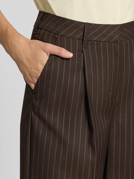 Frauenmodel trägt Wide Fit Hose mit Viskose-Anteil Modell 'Aya Ellis' von JJXX, braunes Nadelstreifen-Design, Nahaufnahme Oberkörper. Elastischer Material-Mix, Bundfalten, Bügelfalten, Haken- und Reißverschluss, Bundweite S/32: 37 cm, Innenbeinlänge S/32: 77 cm.