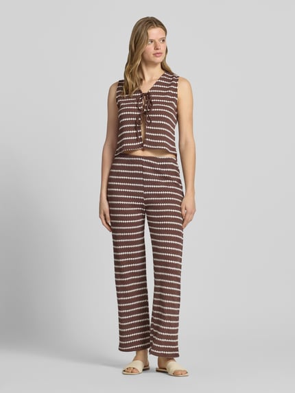 Vrouwenmodel draagt Loose Fit Stoffhose mit Baumwoll-Anteil Modell 'EVA LIFE' van Only met allover-motief, elastische tailleband, gemaakt van gebreide katoenmix, bruin-wit gestreept, flared, textuur oppervlakte, volledige lichaamsaanzicht van voren.