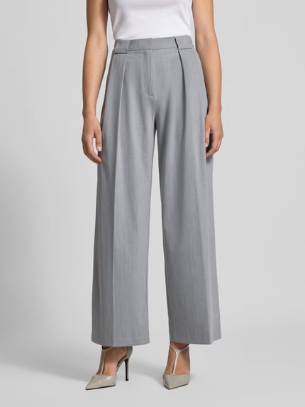 Frauenmodel trägt Fließende Anzughose in Mittelgrau Melange - curated by Viky Rader von Style Icon Collection, Relaxed Fit, Wide Leg, Kellerfalten, Knopf- und Reißverschluss, glatte Textur, Ganzkörperansicht von vorne.