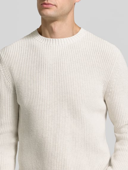 Mężczyzna nosi Regular Fit Strickpullover aus reiner Baumwolle od s.Oliver RED LABEL w kolorze ecru, widoczna faktura dzianiny, nahaufnahme górnej części ciała.