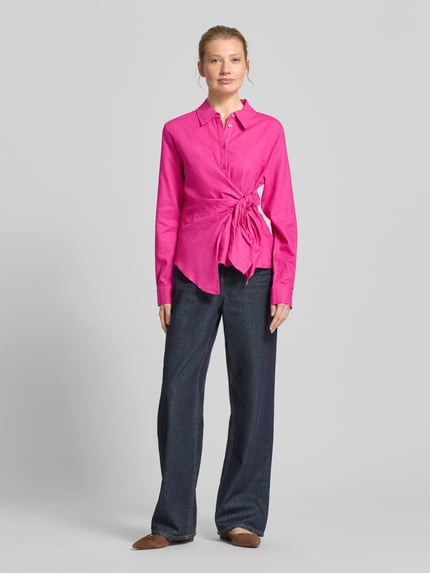Frauenmodel trägt Bluse aus Leinen-Viskose-Mix mit Knoten-Detail Modell 'Mathilda' von GUIDO MARIA KRETSCHMER WOMAN, satter Pinkton, asymmetrischer Schnitt, Hemdblusenkragen, kurze Knopfleiste, Rückenlänge 59 cm, Ärmellänge 63 cm, glatte Textur, Ganzkörperansicht von vorne.