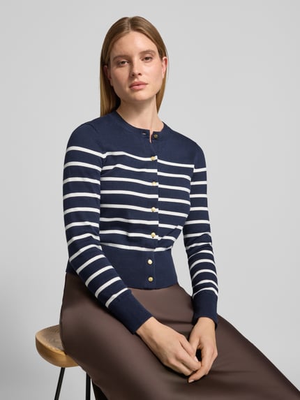 Frauenmodel trägt Cardigan mit goldfarbenen Knöpfen von Tommy Hilfiger in dunkelblauer Strickoptik mit weißen Streifen, Regular Fit, cropped Länge, Rundhalsausschnitt, Feinstrick, Detailknöpfe mit metallischen Akzenten, Ärmel und Rumpf gerippt, Nahaufnahme Oberkörper.