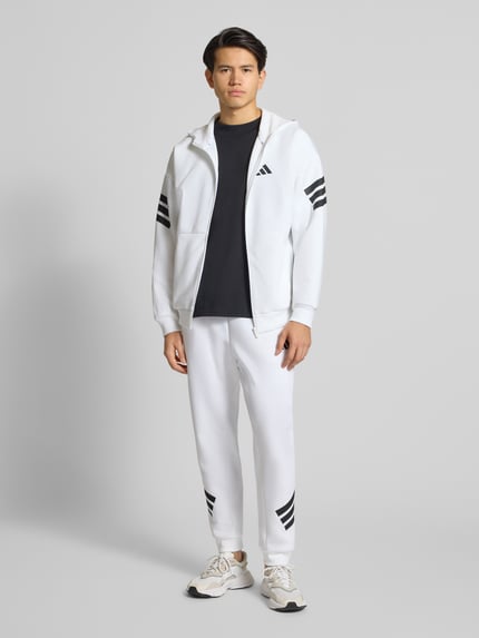 Männermodel trägt Sweatpants mit Logo und elastischem Bund von adidas Sportswear, Weiß mit schwarzen Elementen, Material-Mix mit Baumwoll-Anteil, Regular-Fit, Logo, Elastischer Bund, Tunnelzug, Innenbeinlänge bei Größe M: 71 cm, Ganzkörperansicht von vorne.