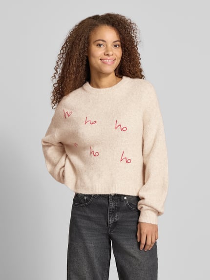 Frauenmodel trägt Relaxed Fit Strickpullover mit Rundhalsausschnitt Modell 'VIXEN' von NOISY MAY®, Woll-Mix, beige mit roten Stichings, Ganzkörperansicht von vorne.