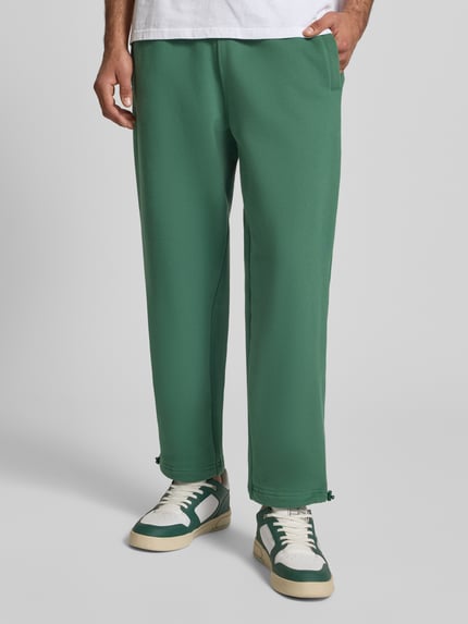 Männermodel trägt Regular Fit Sweatpants mit Gesäßtasche Modell 'Source' von BLKVIS aus reiner Baumwolle in Grün, 7/8-Länge, Nahaufnahme Unterkörper von vorne.