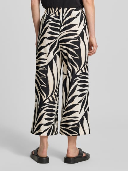 Frauenmodel trägt Wide Fit Stoffhose aus Viskose-Mix Modell 'Life' von Mango mit floraler Allover-Print, Ganzkörperansicht Rückansicht. Damen Stoffhose, Viskose-Mix, Wide-Fit, Modell 'Life', Verkürzte Passform, Elastischer Bund, Bundweite Größe S: 37 cm, Innenbeinlänge Größe S: 60 cm.
