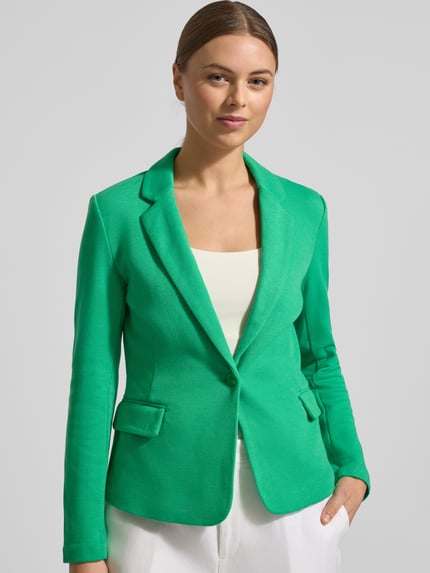 Kobiece modelka nosi Regular Fit Kurzblazer mit Baumwoll-Anteil Modell 'JULIA' von Vero Moda, efekt: jednolity kolor, kołnierz z połami, zapięcie na 1 guzik, długi rękaw, nachodzące na siebie guziki, kieszenie z patką, wykończenie materiału: pika; całkowite ujęcie sylwetki od przodu.