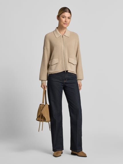 Frauenmodel trägt Strickjacke aus Schurwolle mit Pattentaschen von windsor in Beige, Relaxed Fit, dunkle Jeans, neutrale Farben, Ganzkörperansicht von vorne.