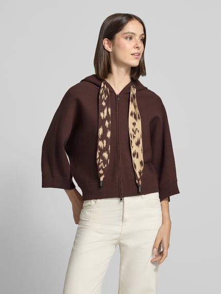 Frauenmodel trägt Strickjacke mit Kapuze von Marc Cain in Braun, Animal Print Kordeln, gestreiftes Innenfutter, Ganzkörperansicht von vorne.