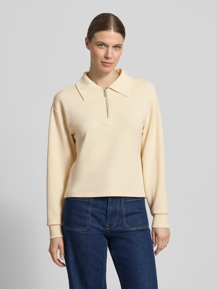 Frauenmodel trägt Sweatshirt mit Reißverschluss von Scotch & Soda aus Material-Mix mit Lyocell-Anteil, Regular-Fit, Umlegekragen, cremefarbene Oberfläche, Ganzkörperansicht von vorne.