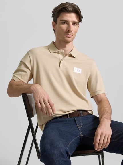 Männermodel trägt Regular Fit Poloshirt mit Knopfleiste von ARMANI EXCHANGE aus Baumwoll-Elasthan-Mix mit Label-Print, Nahaufnahme Oberkörper.