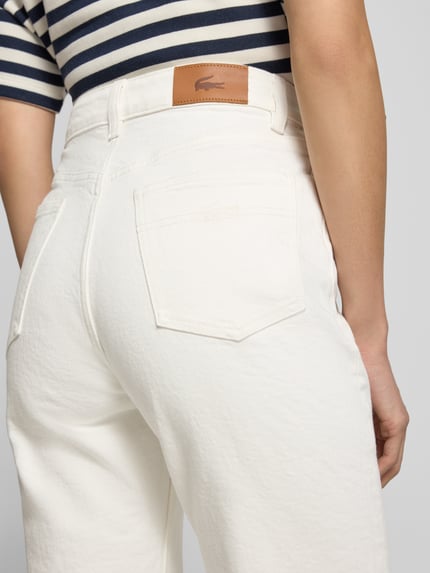 Frauenmodel trägt Straight Fit Jeans aus Baumwoll-Mix von Lacoste in Weiß, sichtbare Gesäßtaschen, Damen Straight Fit Jeans von Lacoste, Ganzkörperansicht Rückansicht.