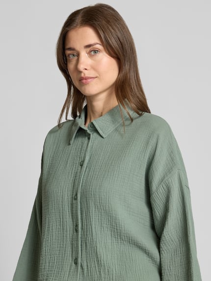 Frauenmodel trägt Loose Fit Hemdbluse aus reiner Baumwolle Modell 'NATALI' von Vero Moda in Optik: Unifarben, Seersucker-Struktur, Knopfleiste, Hemdkragen, 3/4-Arm, Nahaufnahme Oberkörper.