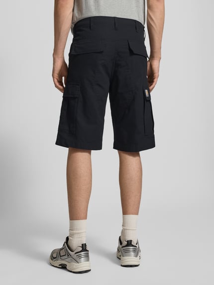 Männermodel trägt Shorts mit Cargotaschen von Carhartt Work In Progress in Dunkelblau mit Gesäßtaschen, Ganzkörperansicht Rückansicht