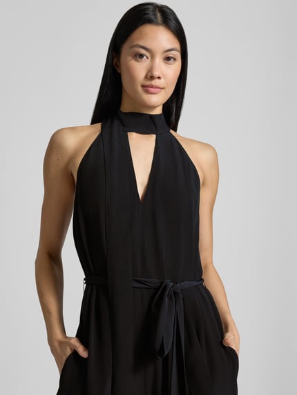 Frauenmodel trägt Regular Fit Jumpsuit aus reiner Viskose Modell 'Chiva' von Ted Baker in Schwarz mit Schlüssellochausschnitt, Nahaufnahme Oberkörper. Damen Jumpsuit, ärmellos, taillierte Passform, Zierschleife, glatte Textur.