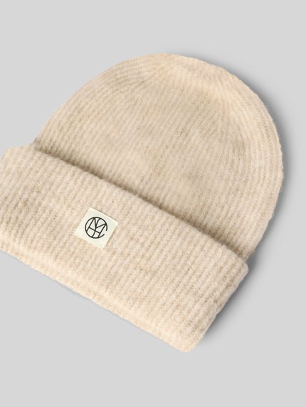 Produktfoto, Mütze aus elastischem Woll-Mix mit Alpaka-Anteil von MSCH Copenhagen in Beige mit breitem Umschlag und Label-Patch auf grauem Hintergrund.