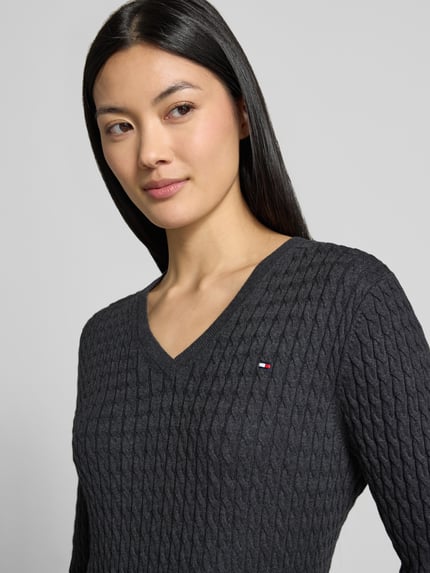 Vrouwenmodel draagt Regular Fit pullover uit puur katoen van Tommy Hilfiger in donkergrijs met kabelstructuur, close-up bovenlichaam. Dames pullover van Tommy Hilfiger