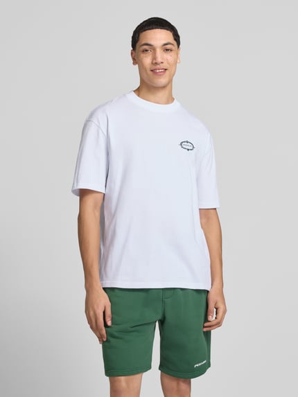 Männermodel trägt Oversized T-Shirt mit rückseitigem Motiv-Print Modell 'Reine' von Pegador in Weiß aus Reine Baumwolle, Label-Print, Rundhalsausschnitt, Oversized-Fit, Herren T-Shirt, Rückenlänge 70 cm bei Größe M, Ganzkörperansicht von vorne.