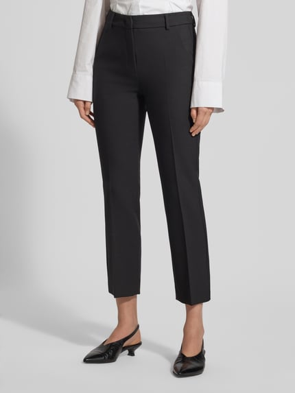 Kobiece model prezentuje spodnie z zakładkami w pasie Slim Fit Bundfaltenhose mit Viskose-Anteil Model 'RANA' od Weekend Max Mara, efekt: jednolity kolor, krój slim fit, wysoki stan, aplikacja: wyhaftowane logo, detale: szlufki na pasek, zapięcie: zamek błyskawiczny z guzikiem i haczykiem, kieszenie: kieszenie z tyłu oraz wpuszczane boczne, wykończenie materiału: tkanina, dodatek wiskozy; widok na całe nogi z przodu.