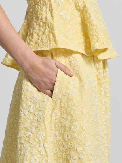 Vrouwenmodel draagt Ausgestellter Maxi-Rock mit Strukturmuster Modell 'FIONA' van Vero Moda in geel met piqué jacquard, regular fit, uni look, zijzakken, detailopname heup.