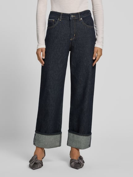 Frauenmodel trägt Raw Denim Jeans mit weitem Umschlag - curated by Viky Rader von Style Icon Collection in Dunkelblau, Wide Fit, 5-Pocket-Design, reine Baumwolle, Knopf- und Reißverschluss, Ganzkörperansicht von vorne.