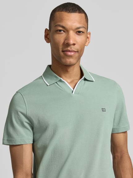 Męski model nosi Modern Fit Poloshirt mit Logo-Stitching od Christian Berg Men z bawełny, kołnierzyk polo, wyhaftowane logo, nowoczesny krój, długość tyłu 71 cm w rozmiarze M, pastelowa zieleń, gładka faktura, zbliżenie na górną część ciała, przód