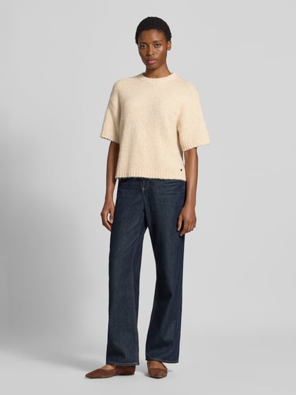 Kobieta modelka nosi sweter z dzianiny Model 'Lotti' od GUIDO MARIA KRETSCHMER WOMAN, mieszanka materiałów z dodatkiem wełny, krój regular fit, okrągły dekolt, rękaw o dł. 1/2, długość tyłu w rozmiarze 36: 56 cm, długość rękawa w rozmiarze 36: 22 cm, jasny beż, gładka tekstura, proste niebieskie spodnie, buty brązowe, całość utrzymana w neutralnych kolorach, widok całej sylwetki z przodu.