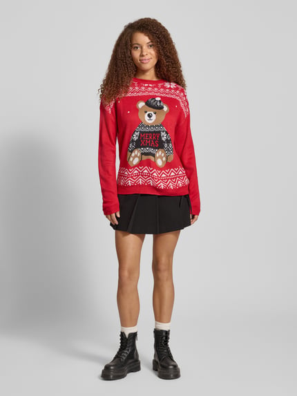 Frauenmodel trägt Regular Fit Strickpullover mit Weihnachtsmotiv Modell 'TEDDY' von Only, unifarben rot, grafisches Muster, gestrickte Textur, Rundhals, lange Ärmel, Ganzkörperansicht von vorne.