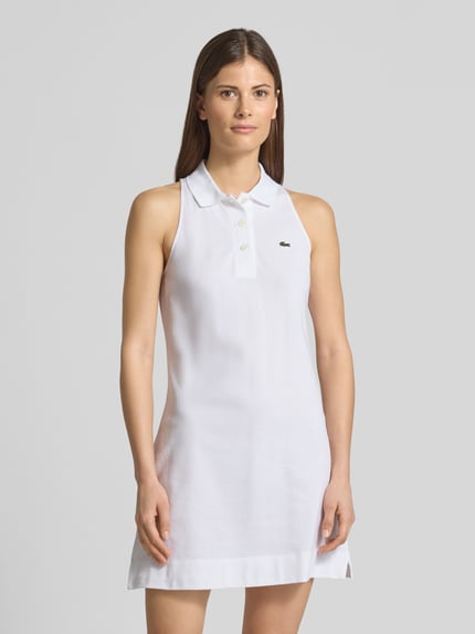 Vrouwenmodel draagt Slim Fit Polokleid aus Baumwoll-Mix van Lacoste, look: effen kleuren, pasvorm: slim fit, minilengte, V-hals, logodetail, korte knoopsluiting, mouwvorm: korte mouw, mouwboord: geribd, zoom: zijsplit, materiaalverwerking: piqué, materiaal: katoenmix. Ganzkörperaanzicht van voren.