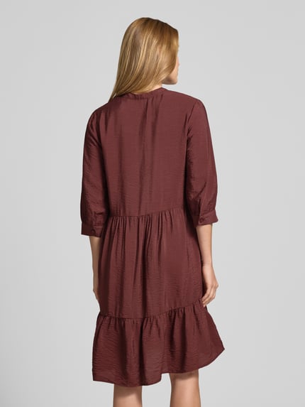 Vrouwenmodel draagt Relaxed Fit Midikleid aus Viskose-Mix mit Tunika-Ausschnitt van Christian Berg Woman, bordeauxrood, knopenlijst, halve mouw, textuur met lichte glans, lengte 106 cm, borstwijdte 45 cm, mouwlengte 44 cm, volledig rugaanzicht.