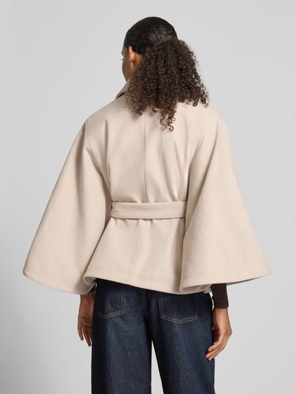 Frauenmodel trägt Loose Fit Poncho mit Bindegurt Modell 'AIKEN' von PIECES, beige, unifarbene Webware, Stehkragen, Ganzkörperansicht Rückansicht.