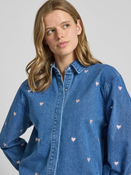 Vrouwenmodel draagt Regular Fit Jeansbluse reiner Baumwolle Modell 'VERA' van Only, denim-look, blauwe twill, hartapplicaties, V-hals, lange mouwen, knoopsluiting, hemdkraag, rugpas, detailopname bovenlichaam.