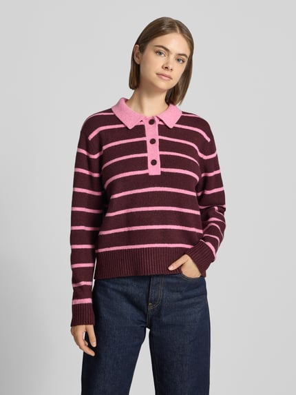 Frauenmodel trägt Strickpullover mit Polokragen Modell 'RUBY' von JJXX, bordeaux mit rosa Streifen, lockere Passform, Ganzkörperansicht von vorne. Material-Mix mit Baumwoll-Anteil, gerippte Abschlüsse, Rückenlänge 48 cm, Ärmellänge 59 cm.