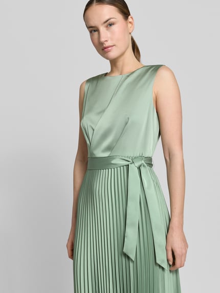 Frauenmodel trägt Midikleid mit Plisseefalten und Bindegürtel von comma in Mintgrün, fließender Material-Mix, Nahaufnahme Oberkörper.
