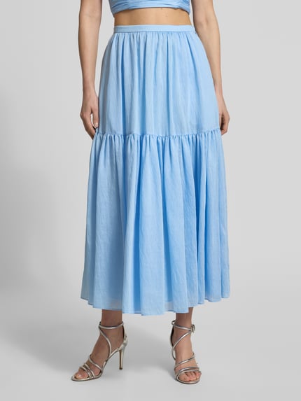 Frauenmodel trägt Maxirock mit Volantsaum und seitlichem Reißverschluss von Jake*s Cocktail in Hellblau, A-Linie, Ganzkörperansicht von vorne. Bundweite 35 cm, Gesamtlänge 90 cm bei Größe 36.