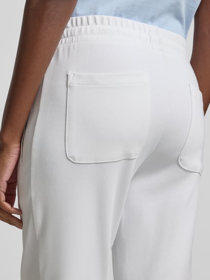 Vrouwenmodel draagt Sweatpants aus Baumwoll-Mix van Juvia in wit, elastische tailleband, achterzak, detailopname achteraan. Elastische katoen-modal mix, taps toelopende pijp, steekzakken, elastische boorden, binnenbeenlengte maat S 42 cm, taillewijdte maat S 67 cm.