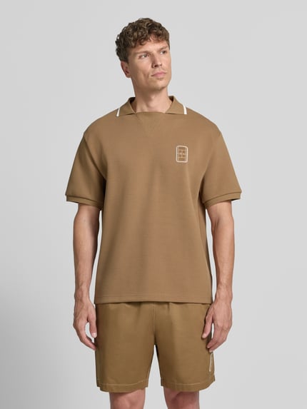 Männermodel trägt Loose Fit Poloshirt von Lacoste in Braun mit Kurzarm und strukturierter Textur, Ganzkörperansicht von vorne. Herren Poloshirt.
