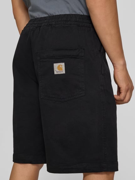 Männermodel trägt Shorts aus Baumwoll-Mix Modell 'Floyde' von Carhartt Work In Progress in Schwarz, lockerer Schnitt, Ganzkörperansicht Rückansicht. Relaxed Fit, elastischer Bund, Eingrifftaschen, sichtbares Logo-Patch.