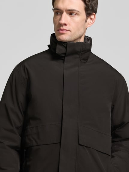 Männermodel trägt Jacke mit Kapuze und Pattentaschen Modell 'LAMOON' von JACK & JONES in Schwarz, Regular Fit, Nahaufnahme Oberkörper. Rückenlänge 72 cm, Schulterbreite 50 cm, Brustweite 60 cm, Ärmellänge 65 cm, verdeckter Reißverschluss.