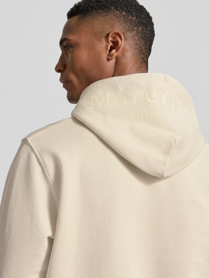 Männermodel trägt Regular Fit Hoodie aus reiner Baumwolle von Marc O'Polo in Beige mit Kapuze, Label-Schriftzug, Nahaufnahme Rückansicht.