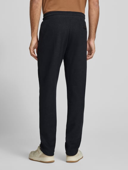 Mężczyzna nosi Sweatpants mit elastischem Bund und Tunnelzug von bugatti w kolorze czarnym, bawełniany miks, krój regular fit, długość nogawki wewnętrznej w rozmiarze M: 80 cm, widok całej sylwetki od tyłu.