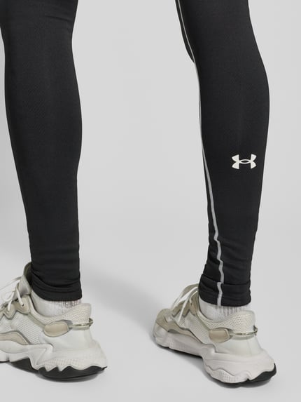 Mężczyzna nosi Leggings mit elastischem Bund und Label-Details od Under Armour, czarny materiał ze stretchem, widoczne logo, zbliżenie na nogi.