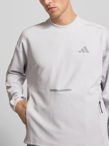Männermodel trägt Regular Fit Sport-Langarmshirt mit Lyocell-Anteil von adidas Training in hellem Grau, dezente Struktur, Nahaufnahme Oberkörper.