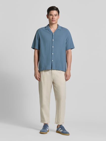 Männermodel trägt Relaxed Fit Freizeithemd aus reiner Baumwolle Modell 'RLXCAL' von SELECTED HOMME in Blau mit Bowling-Kragen, Ganzkörperansicht von vorne.