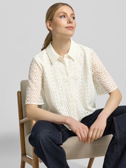 Frauenmodel trägt Regular Fit Hemdbluse in Spitzen-Optik von comma, semitransparent mit Hemdblusenkragen und Halbarm, Nahaufnahme Oberkörper.